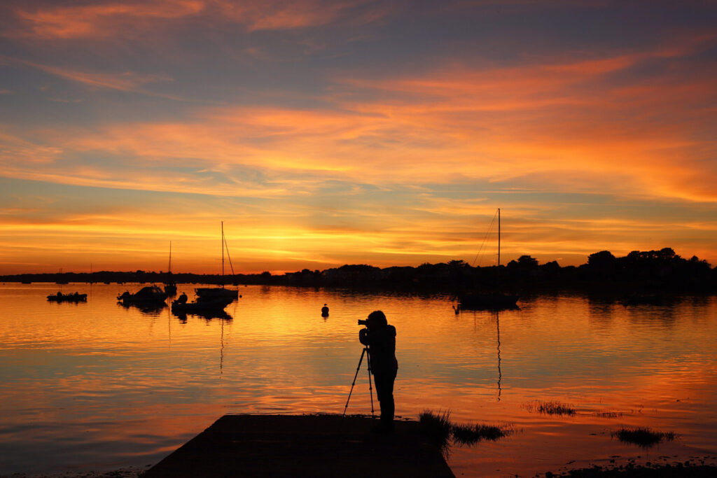 Sunset sky over river estuary with a photographer silhouetted in the foreground