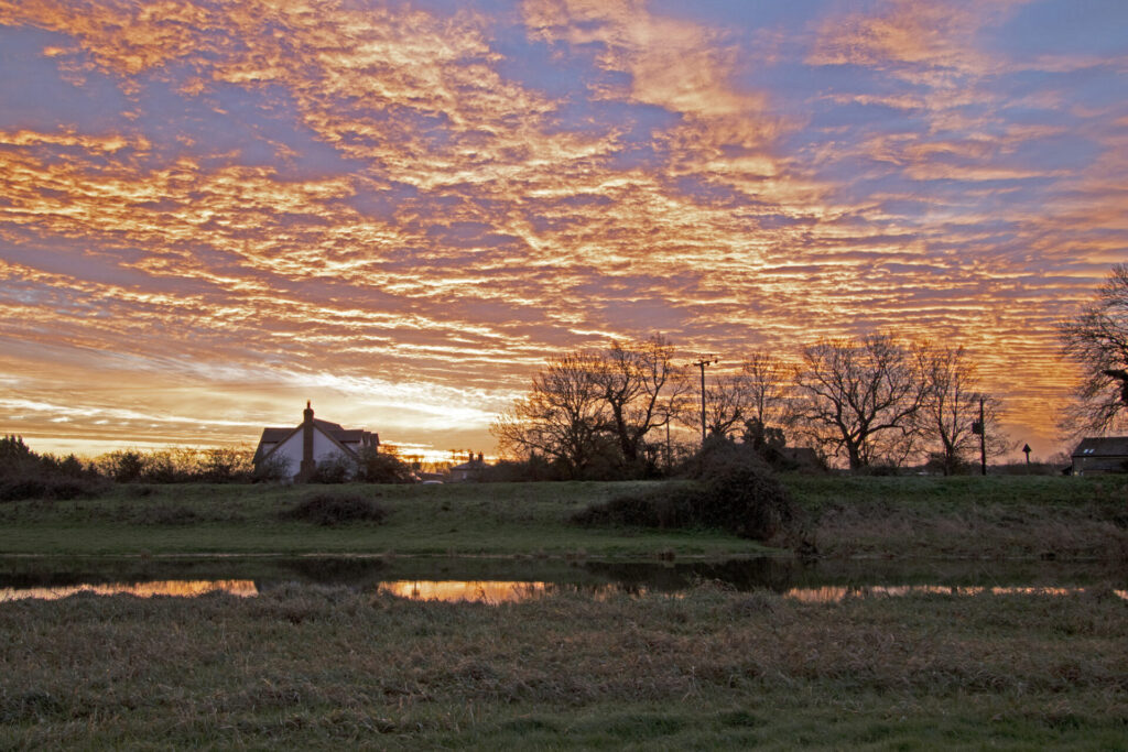Sunset sky and clouds over Fenland river with house and trees in distance