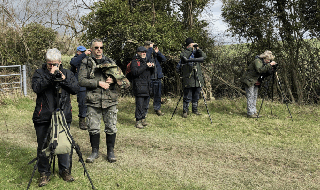 Members of Bird Watching looking with cameras and binoculars at unseen birds to the right